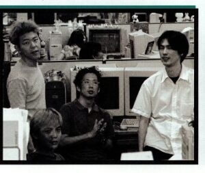 Four Japanese team members gathered around a set of computers, looking towards the camera.